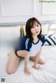 A woman in a blue and white shirt is sitting on a bed.