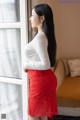 A woman in a red lace skirt looking out a window.