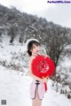 A woman in a pink dress holding a red heart in the snow.