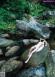 A naked woman laying on a rock in a stream.