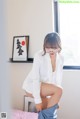 A woman in a white shirt and blue skirt sitting on a bed.