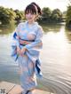 A woman in a blue kimono standing by a body of water.