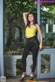 A woman in a yellow top and black pants posing for a picture.