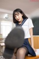 A woman in a school uniform sitting on a desk.