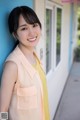 A woman leaning against a blue wall smiling at the camera.