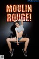 A woman sitting on a chair in front of a sign that says Moulin Rouge.