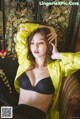A woman in a yellow jacket and black bra sitting on a couch.