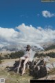 A woman sitting on top of a rock holding an umbrella.