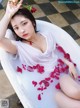 A woman sitting in a bathtub with rose petals on the floor.