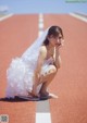 A woman in a wedding dress crouching down on a track.