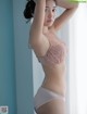 A woman in a pink bra and panties leaning against a window.