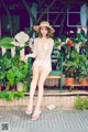 A woman sitting on a bench in a white dress and hat.